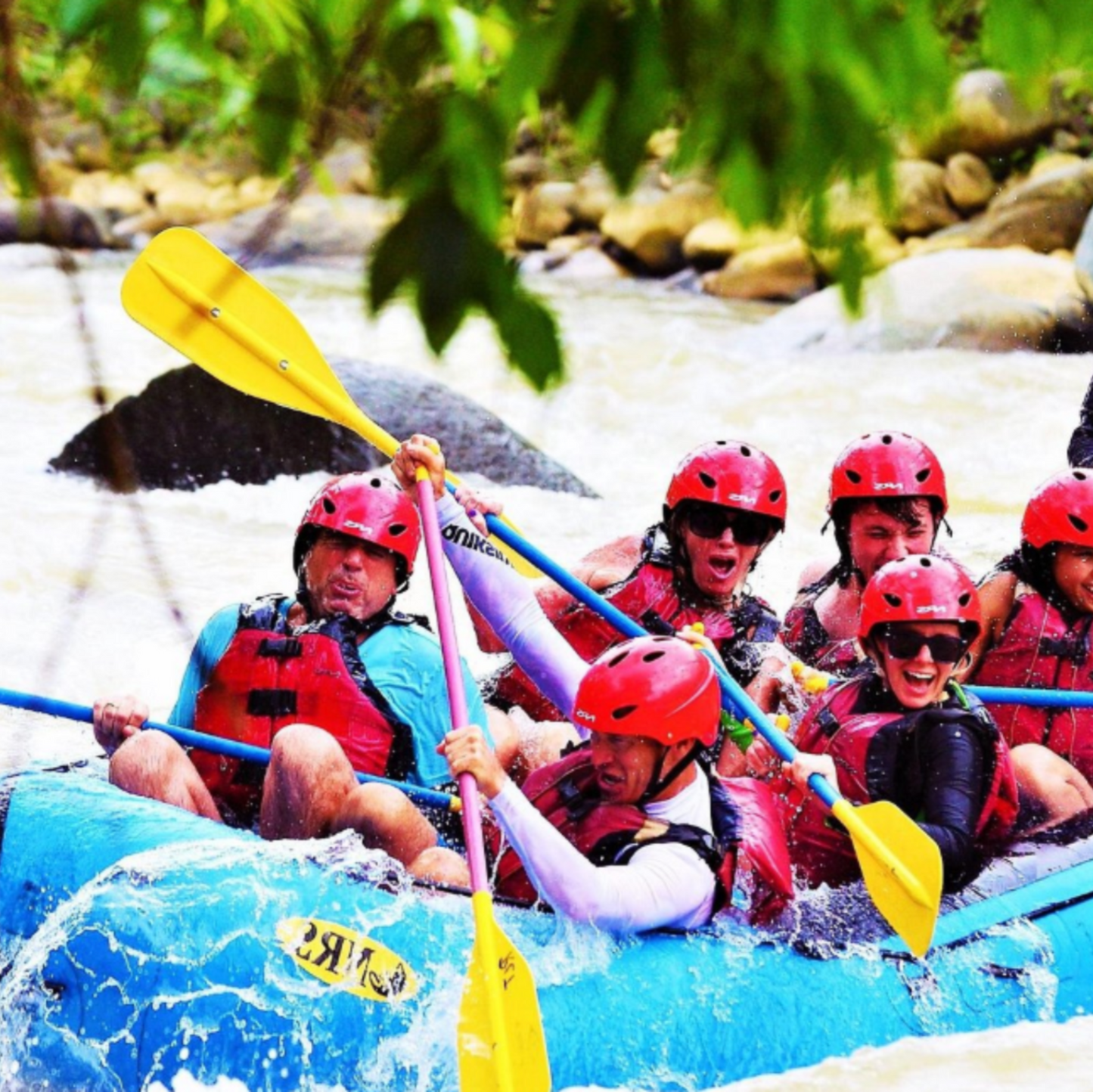 Group of people white water rafting with helmets and life jackets on a river.